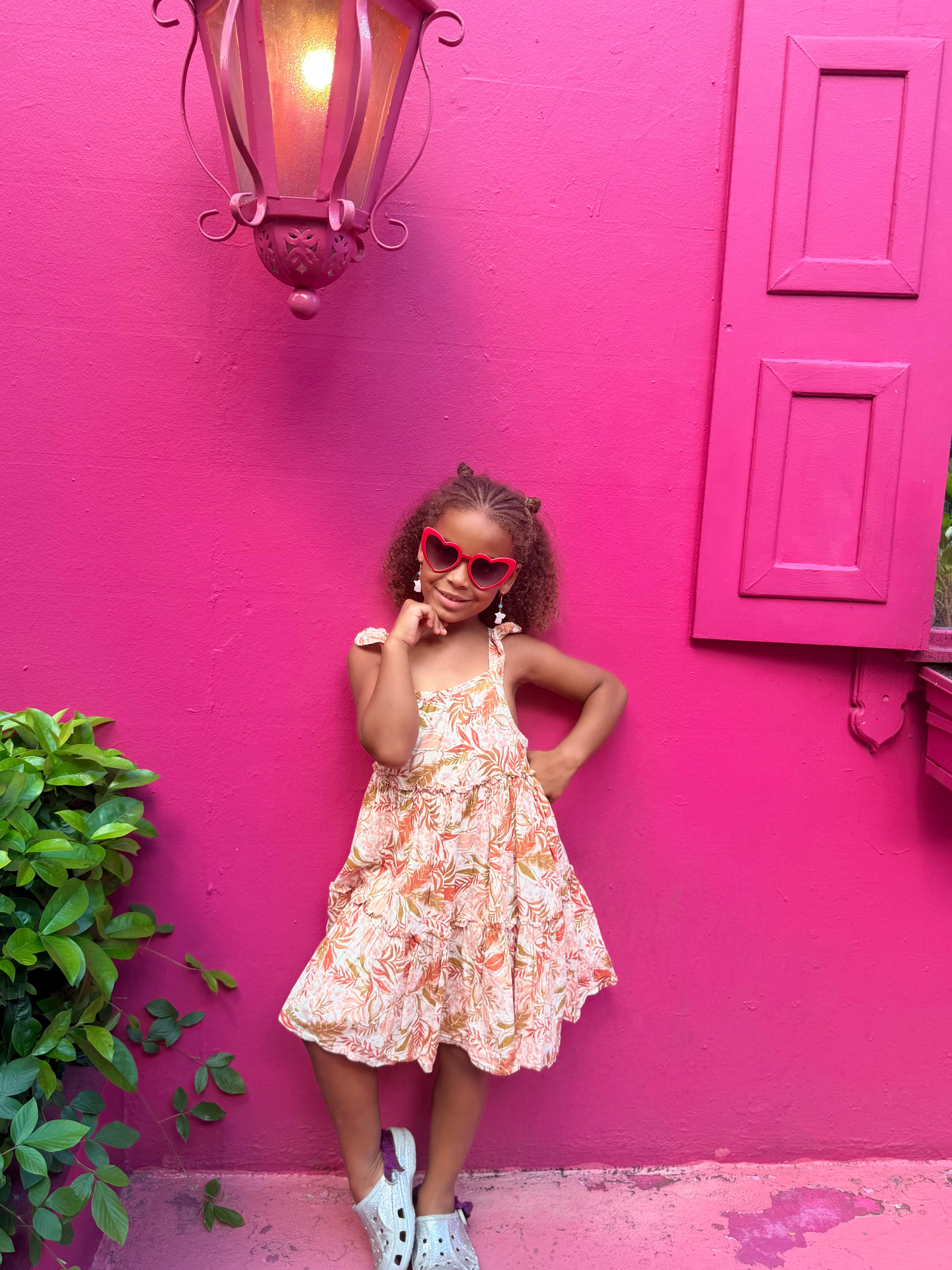 Kemi, age 6, in heart-shaped sunglasses against a pink wall